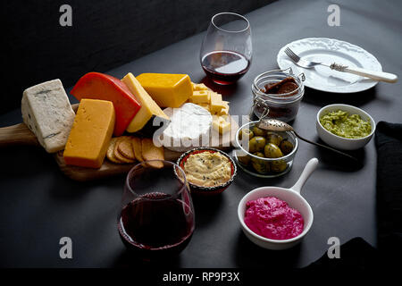 Wooden board with various types of cheese and snacks and two glasses of red wine on black smooth table Stock Photo