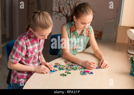 Two little girls solving puzzle together sitting at the table Stock Photo