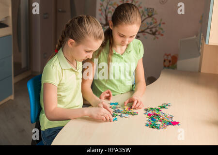 Two little girls solving puzzle together sitting at the table Stock Photo