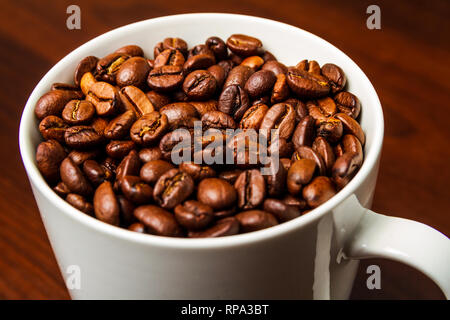Roasted Coffee beans in a white mug cup isolated on a rustic wood table Stock Photo