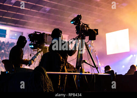 A group of cameramen working during the concert. Television broadcast event. Silhouettes of workers against the background of colorful beams. Stock Photo