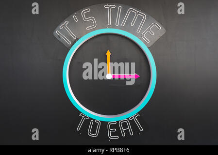Neon concept clock sign showing 'Eat Time'. Maket clock on black wall indicating time for meal. Stock Photo