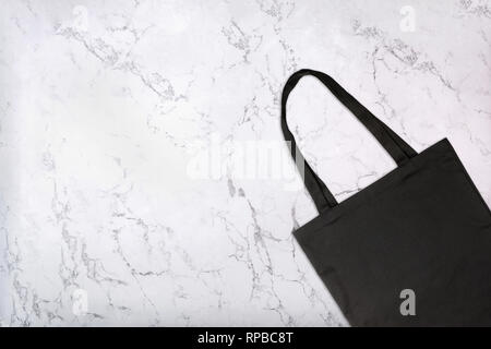 Closeup of black tote bag on white marble texture. Blank reusable shopping bag on marble background. Top view Stock Photo