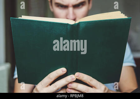 The man enjoys reading the green book. Book closeup in the hands of a young guy. The surprise on her face. Stock Photo