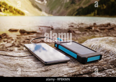 Portable solar panel for charging mobile devices lying on a log in the mountains where there is no electricity Stock Photo