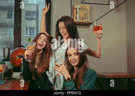 Female friends having a drinks at bar. They are sitting at a wooden table with cocktails. They are wearing casual clothes. Stock Photo