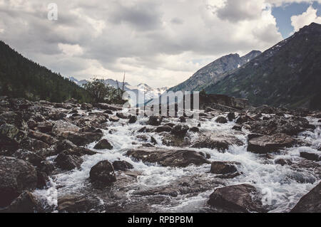 Clear river with rocks leads towards mountains. The river flows into the lake Stock Photo