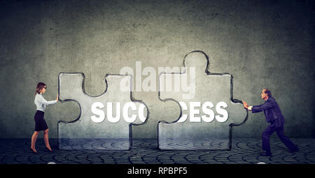 Two business people man and woman working together in tandem to put up two puzzle pieces in order to succeed Stock Photo