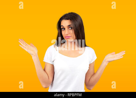 Portrait of a confused young casual girl shrugging shoulders isolated on yellow background