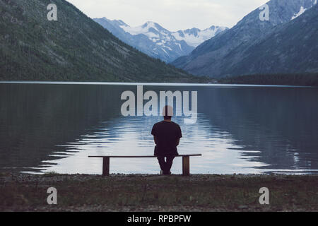 Man sitting on bench overlooking like. The concept of loneliness. Stock Photo