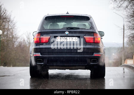 GRODNO, BELARUS - OCTOBER 2016: BMW X5 back view with glowing red backlights standing on asphalt under rain covered with raindrops over gray rainy sky Stock Photo