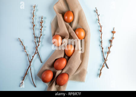 Easter eggs on beige textile with willow branches on pale blue background. Easter card. Stock Photo