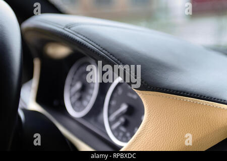 Speedometer and tachometer on dashboard of an luxury car closeup, covered with natural beige and black stitched leather. Stock Photo