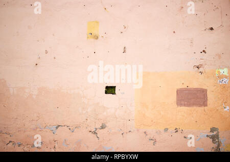 a small rectangular window, a wall of an old building covered with beige plaster and inscriptions of vandals, painted over with orange paint in the fo Stock Photo
