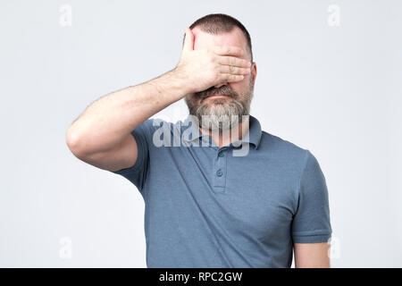 Man in blue t-shirt covering his face with hands Stock Photo