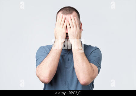 Man in blue t-shirt covering his face with hands Stock Photo