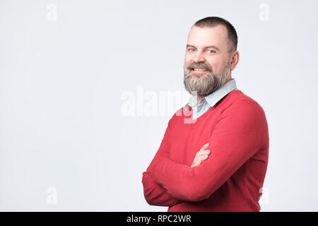 Mature man with beard holding hands crossed and looking at camera while smiling Stock Photo