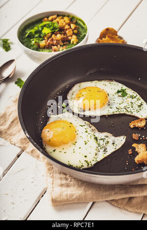 two fried eggs in a pan with herbs and salt for spinach, top view Stock Photo
