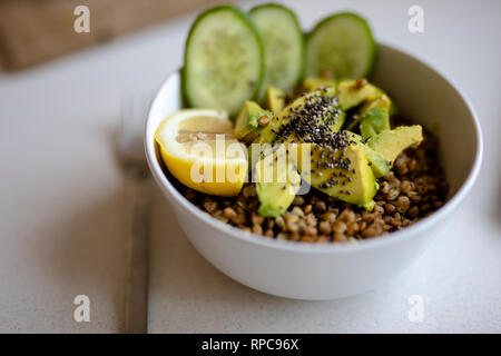 Cooked Buckwheat with avocado and Cucumbers, and Chia seed served in a bawl for breakfast. Gluten free meal. Fresh green vegetables ready on cutting b Stock Photo