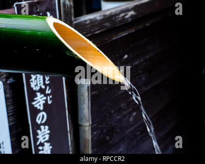 A bamboo pipe pours overflow water out of a Japanese hot spring bath on the side of Oyama, a mountain in Isehara, Kanagawa Prefecture, Japan Stock Photo