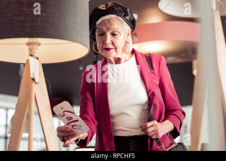 Bewitching elegant senior lady looking at sale sign in hand
