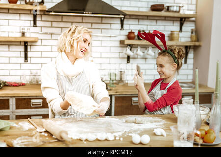 Amused young girl making photo of her mother during working process Stock Photo