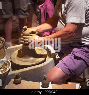 Potter makes a clay pot, sitting outside surrounded by people watching his work Stock Photo