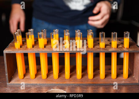 Photo of test tubes with orange liquid and hands of men. Stock Photo