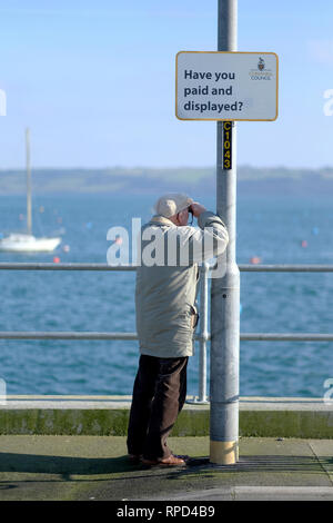 A retired man by the sea looking through binoculars Stock Photo