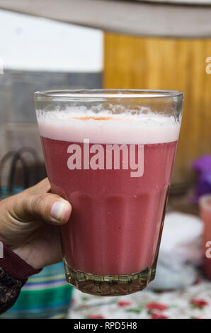 A male hand holding a glass cup with strawberry juice bought at the Pisac market in Cusco - Peru Stock Photo