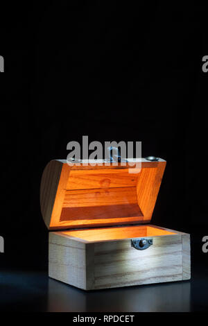 Small wooden chest inside illuminates against a black background with spotlight on the lock. Stock Photo