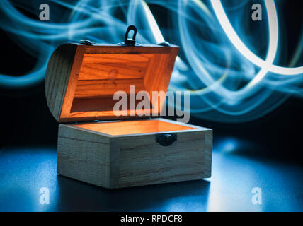 Small wooden chest inside illuminates on a blue background with circular light tracks in front of a black backdrop. Stock Photo