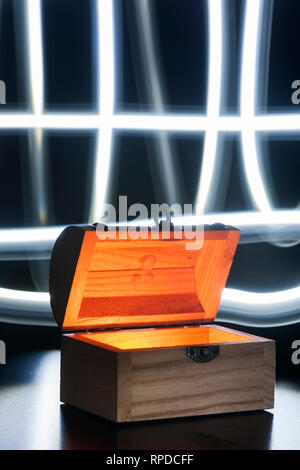 Small wooden chest inside illuminates on a blue background with crossed light-tracks in front of a black backdrop. Stock Photo