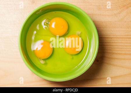 Three raw eggs in a green cup in top view. Stock Photo