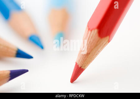 Close-up of blue crayon tips arranged semicircularly around a red colored pencil on white. Stock Photo