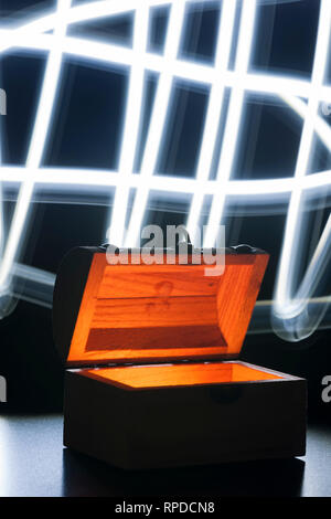 Small wooden chest inside illuminates on a blue background with crossed light-tracks in front of a black backdrop. Stock Photo