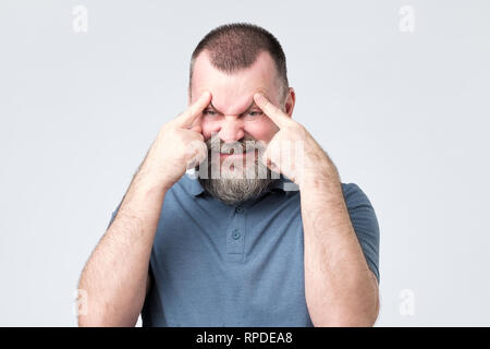 Man with beard holds fingers on temples, trying to remember something. Stock Photo