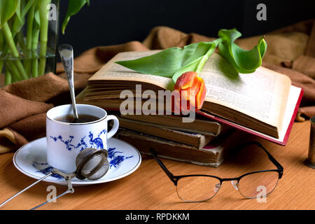 Red tulip on the old book next to a cup of tea Stock Photo