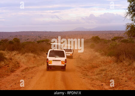 Several safari cars in Kenya in Africa, red sand and mountains in the background Stock Photo
