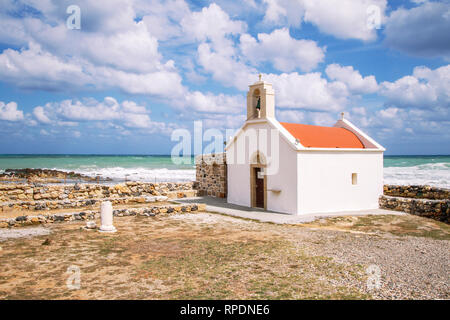 White Greek Agios Nikolaos Church with red roof by the beach on the background of beautiful clouds and Mediterranean Sea. Crete Island. Greece Stock Photo