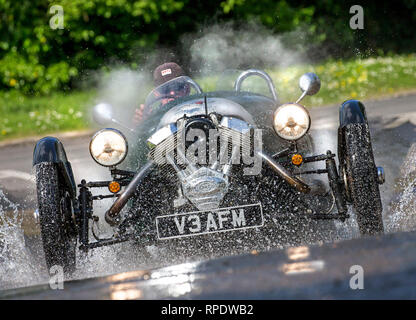 Morgan 3-Wheeler splashing through a ford at speed with headlights on and reflections in the wet road. Model Release form signed. Stock Photo