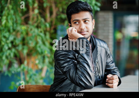 Portrait of stylish and casual young asian man wear on leather jacket spending time at cafe and speaking on mobile phone. Stock Photo