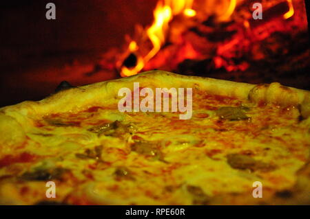 Professional pizza oven with wood burning in background.Rustic pizza in wood fired oven. Stock Photo