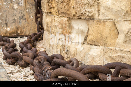 A huge, old and rusty chain hanging down from sandstone wall in Fort St. Elmo, Valletta, Malta. Stock Photo