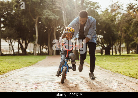 Boy learning to ride a bicycle with his father in park. Father teaching his son cycling at park. Stock Photo