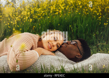 Young interracial couple lying on the grass in meadow. Relaxed young man and woman lying on the grass outdoors. Stock Photo