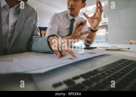 Two businessmen working together over statistical charts at coffee shop. Business people discussing new plan for their project using some statistical  Stock Photo