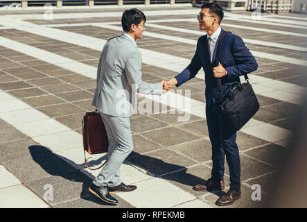 Two asian businessmen shaking hands outdoors in the city. business people greeting each other outdoors. Stock Photo