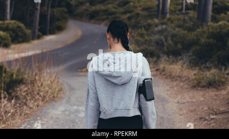 Rear view shot of young woman walking on country trail. Fitness woman in sportswear on cross country path. Stock Photo