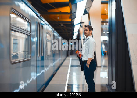 Young attractive businessman waiting for train in metro or subway on modern stylish platform. Concept of commuting. Stock Photo